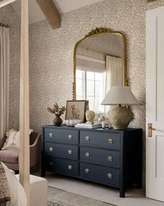 a bedroom with a dresser, mirror and lamp on it's side table in front of a window