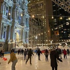 people skating on an ice rink in front of a large building with lights strung from it