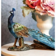 a statue of a peacock sitting on top of a table next to a vase filled with flowers