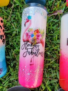 three water bottles with flamingos painted on them sitting in the grass next to each other