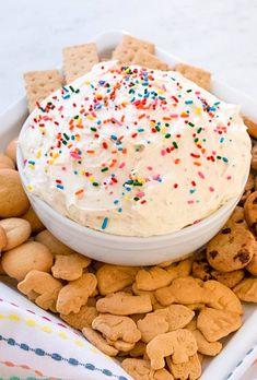 a bowl filled with white frosting surrounded by crackers and sprinkles