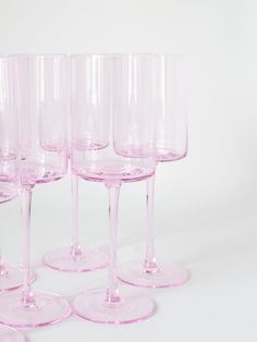 five pink wine glasses are lined up on a white surface, with one empty glass in the middle