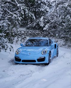 a blue sports car parked in the snow next to some evergreens and trees covered in snow