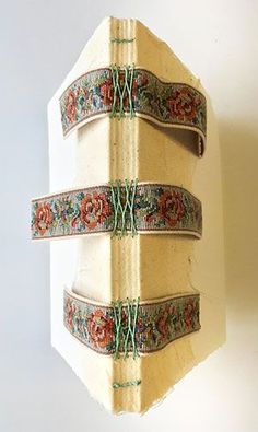 an old book with decorative ribbons hanging from it's sides on a white wall