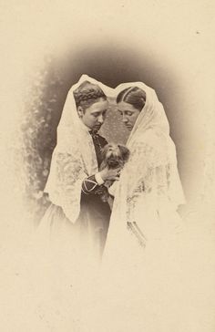 an old black and white photo of two women dressed in wedding attire, one holding a small dog