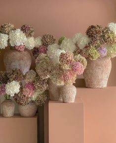 three vases filled with flowers sitting on top of each other in front of a pink wall