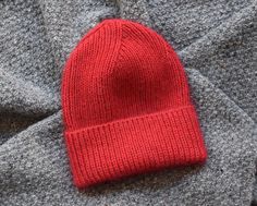 a red knitted hat laying on top of a pile of gray woolen blankets