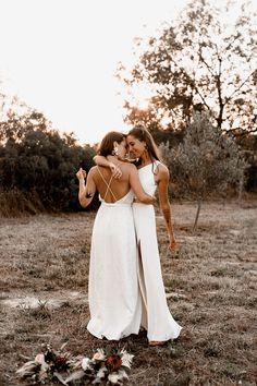 two women in white dresses standing next to each other with their arms around each other