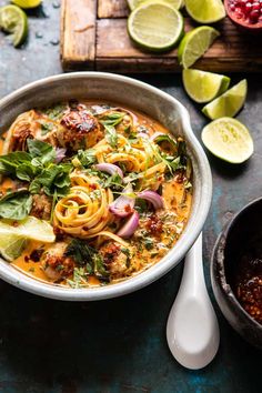 a bowl filled with noodles, meat and vegetables next to sliced limes on a cutting board