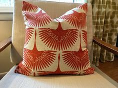 a red and white pillow sitting on top of a wooden chair next to a window