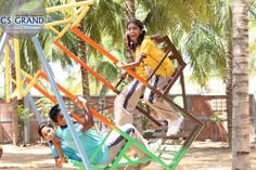 two children are playing on a colorful swing set with palm trees in the back ground