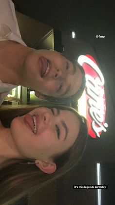 two people standing next to each other in front of a coca cola sign