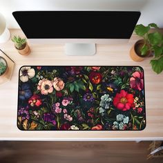 a computer desk topped with a monitor and flower mouse pad next to a potted plant