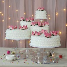 three tiered white wedding cake with pink flowers on top and cupcakes in the middle