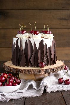 a cake with chocolate and cherries is on a wooden stand next to some cherries