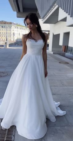 a woman in a white wedding dress is standing on the sidewalk and looking at something