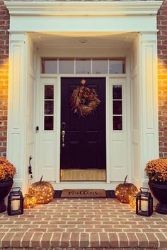 two pumpkins sitting in front of a black door with lights on the side and an autumn wreath hanging over it