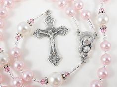 a rosary with pink pearls and a silver cross on the end is laying on a white surface