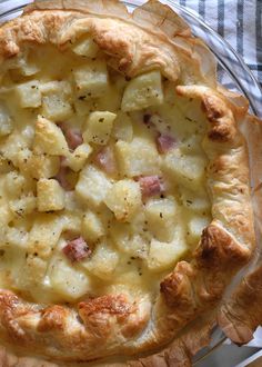 a pie with potatoes and ham in it sitting on a glass plate next to a fork