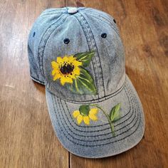 a denim cap with yellow flowers painted on it sitting on a wooden floor next to a pair of scissors