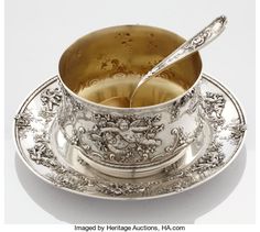 an ornate silver cup and saucer with spoon