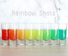 seven glasses filled with different colored liquids on a table