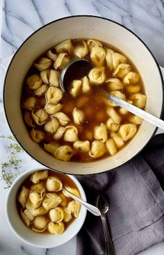 two bowls filled with macaroni and cheese soup on top of a marble table