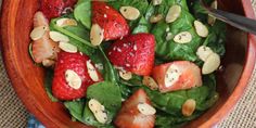 a salad with spinach, strawberries and almonds in a wooden bowl on a table