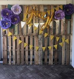 some purple and yellow paper flowers are on a pallet with the word yay spelled out