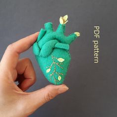 a hand holding a small stuffed animal in the shape of a heart with leaves on it