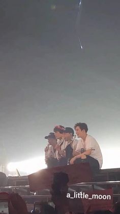 three men sitting on top of a stage with microphones in their hands and people standing around