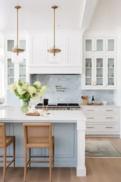 a kitchen with white cabinets and wooden chairs in front of an island counter topped with flowers