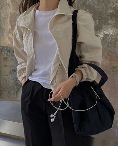 a woman in white shirt and black pants holding a bag with ear buds on it