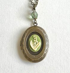 "Here is a very pretty lily of the valley locket necklace, featuring an oval shaped brass locket which is embellished with a sage green floral cameo in the center. This locket is suspended from a pale green, Czech glass bead  and comes on a soldered brass chain and is closed with a solid brass clasp. Perfectly sweet gift, this necklace comes shipped in a gift box! Locket measures: 7/8\" across x 1 1/4\" long Necklace chain length - please choose from the drop down menu. Locket comes shipped in a Vintage Lily Of The Valley, Necklace Locket, Sage Green Floral, Vintage Locket, Picture Locket, Vintage Lockets, Necklace Chain Lengths, Necklace Green, Bird Jewelry