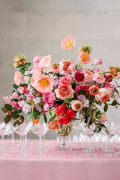 a vase filled with lots of flowers on top of a table covered in wine glasses