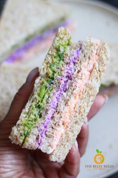 a hand holding a half eaten sandwich on top of a white plate with purple and green sprinkles