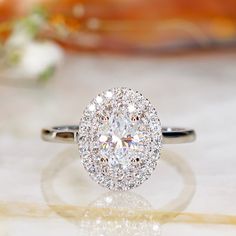 a diamond ring sitting on top of a white surface with flowers in the back ground