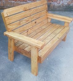 a wooden bench sitting in front of a brick wall and cement floored area with no one on it