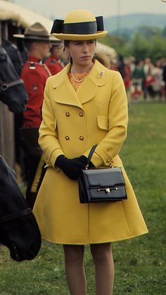 a woman in a yellow coat and hat standing next to a black horse