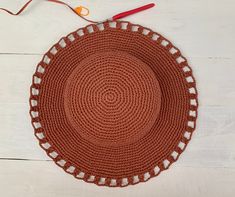 an orange crocheted placemat next to scissors and yarn on a white wooden surface