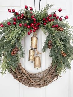 a wreath with bells hanging from it and evergreen branches on the front door, decorated with red berries and pine cones