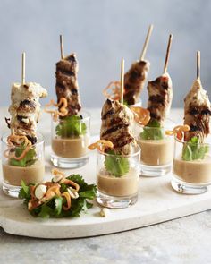 several skewered meats with sauce and garnishes in small glass cups