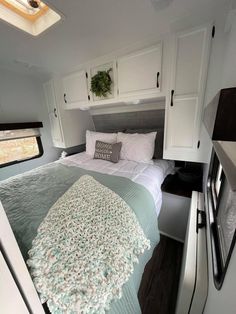 a bed in the back of a trailer with white cupboards and pillows on it