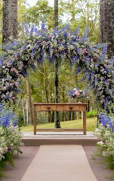 an outdoor ceremony with blue flowers and greenery on the altar, surrounded by tall trees