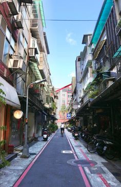 a narrow city street lined with buildings and parked scooters on both sides in front of them