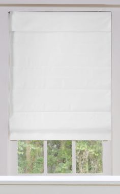 a window with white roman shades on the windowsill and trees in the back ground