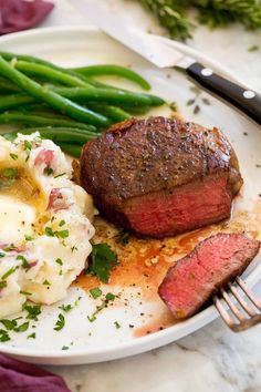 a steak, mashed potatoes and green beans on a white plate with a fork