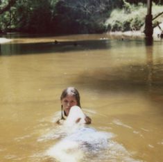 a girl in the water with a frisbee near her face and trees behind her