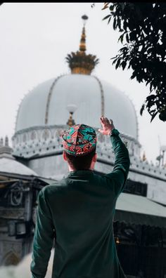 a man standing in front of a white building with a green hat on his head