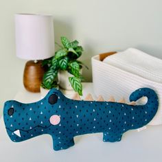 a blue toy alligator sitting on top of a table next to a lamp and potted plant